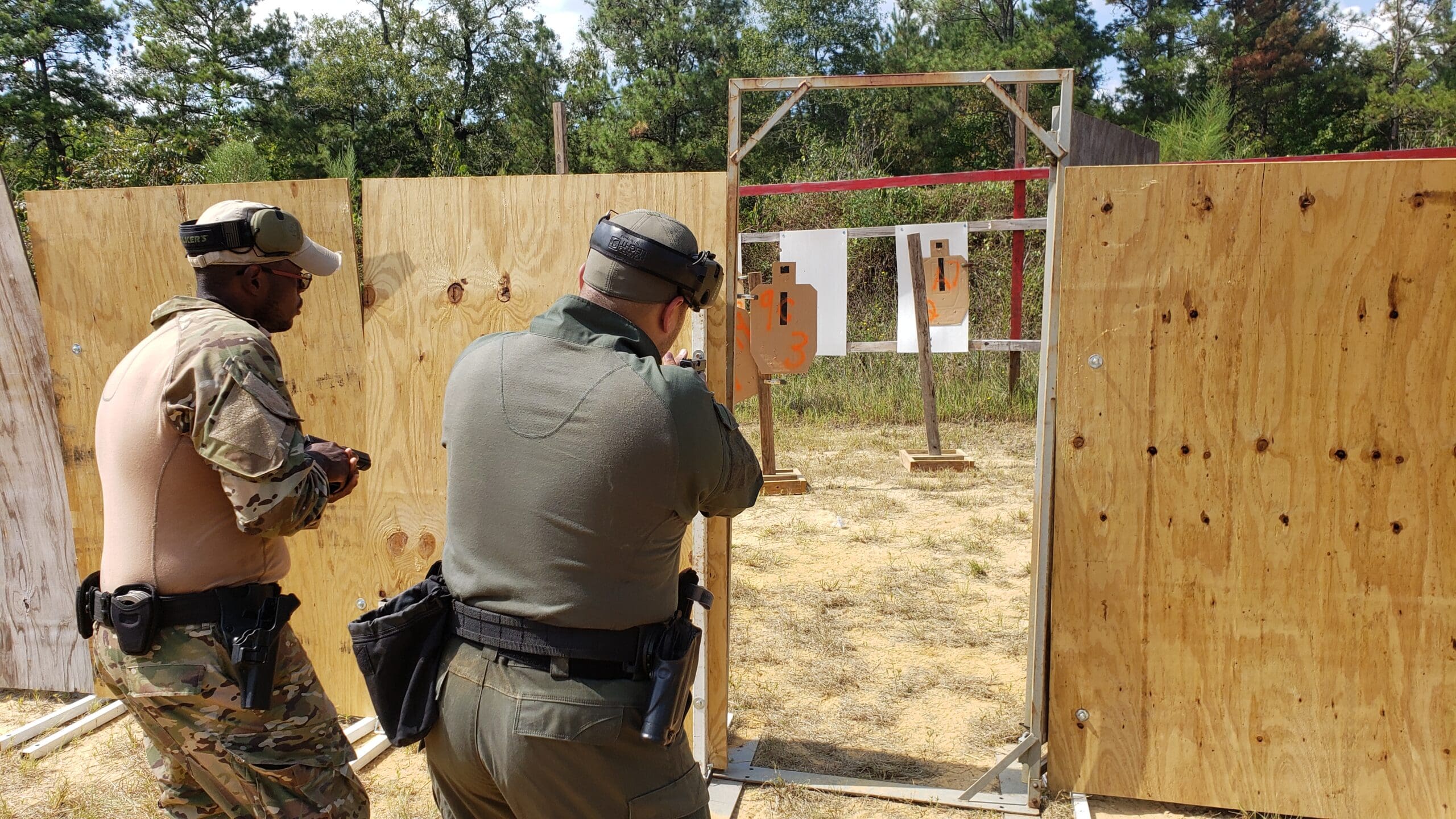 Two individuals in tactical gear practice shooting at paper targets on a range.