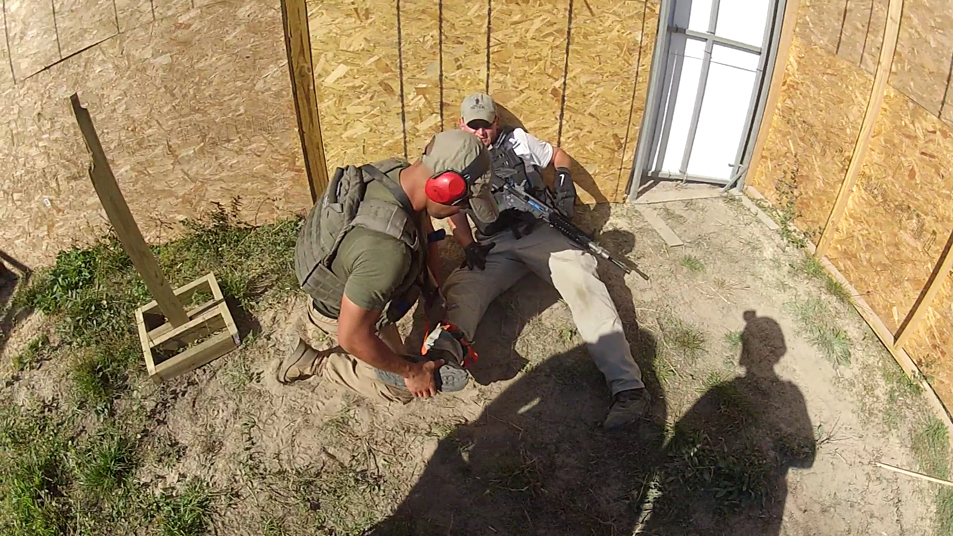 Two men are in a simulated tactical training scenario inside a plywood structure.