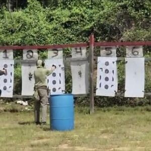 Seven people practice shooting at a firing range, aiming at numbered targets.