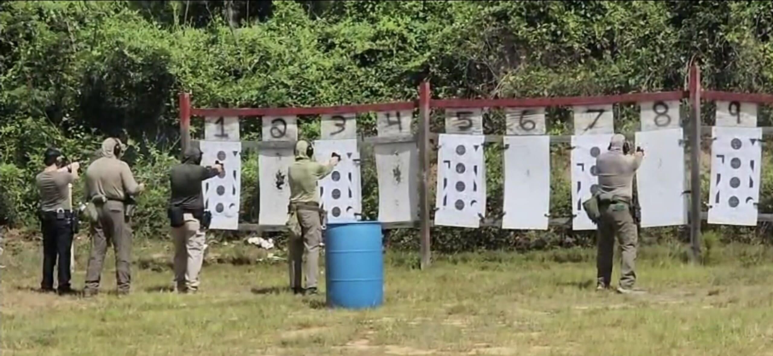 Seven people practice shooting at a firing range, aiming at numbered targets.
